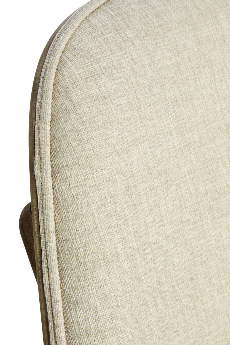 Close-up of a light beige textured fabric cushion with a curved edge and a small portion of a brown frame or backing visible on the left side, set against a plain white background.