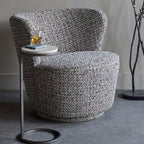 Gray textured armchair with a small round table on a gray floor.