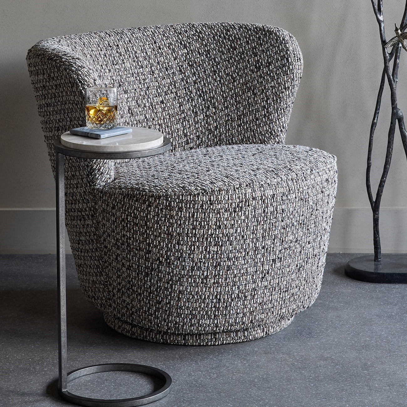 Gray textured armchair with a small round table on a gray floor.