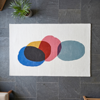 Colorful abstract rug on a dark gray tiled floor with a plant in the corner.